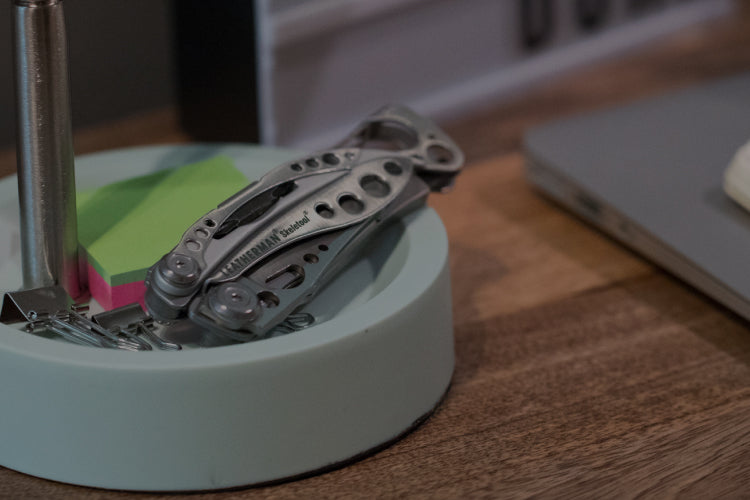Translation missing: de.Stainless Steel Leatherman Skeletool® resting on a desk organizer beside a notebook and sticky notes in a modern workspace.