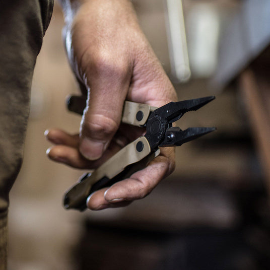 Translation missing: de.Hand holding Coyote Rebar with pliers open with a blurred workshop background