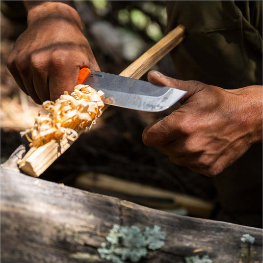 Translation missing: pl.Person using a Leatherman Pioneer knife to carve feather sticks from a wooden branch in an outdoor setting, shown in a close-up highlighting controlled bushcraft technique