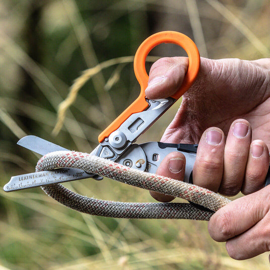 Translation missing: pl.A man using an orange and black Leatherman Raptor Rescue shears to cut a thick rope