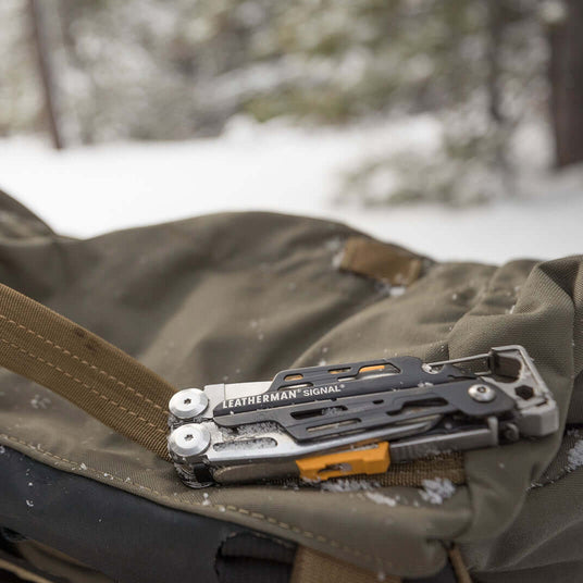 Translation missing: pl.A gray Leatherman Signal closed on a backpack surrounded by snow