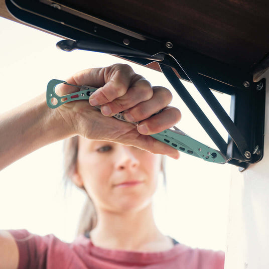 Translation missing: de.Person using a Leatherman Skeletool CX multi-tool to adjust hardware on a lift mechanism, shown in a close-up with focus on the tool in a compact, lightweight design