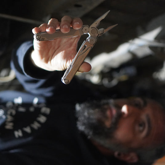 Man using a leatherman Wave+ while under a van.
