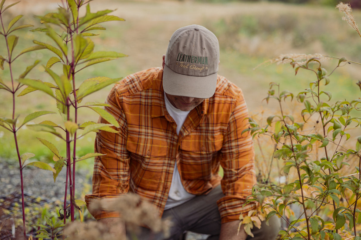 Translation missing: es.A person wearing a driftwood colored Leatherman Dad Hat tending to plants outdoors while dressed in an orange plaid shirt