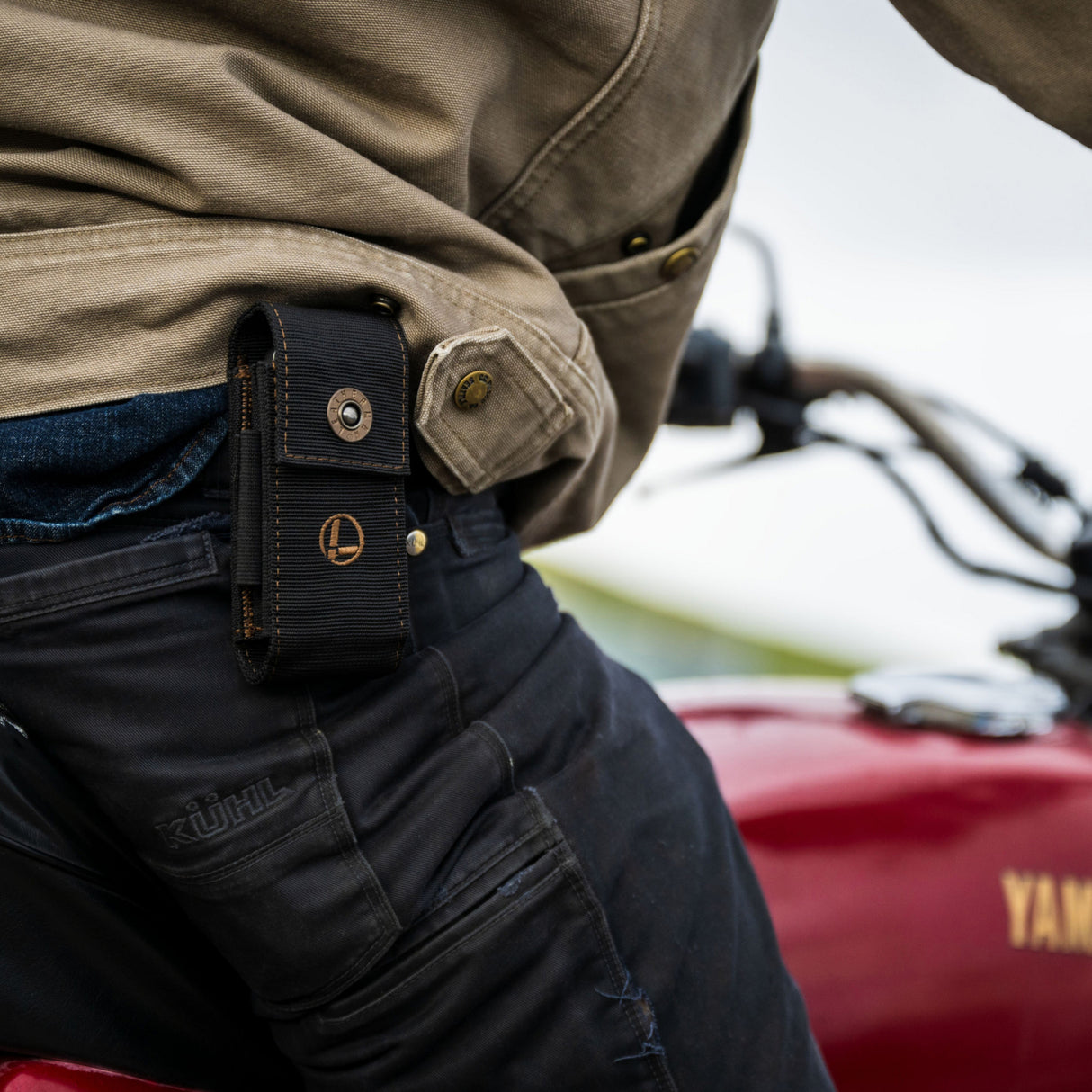 Translation missing: de.A man riding a motorcycle, wearing the Leatherman Black Bronze Nylon Sheath on his side, cruising down a scenic road