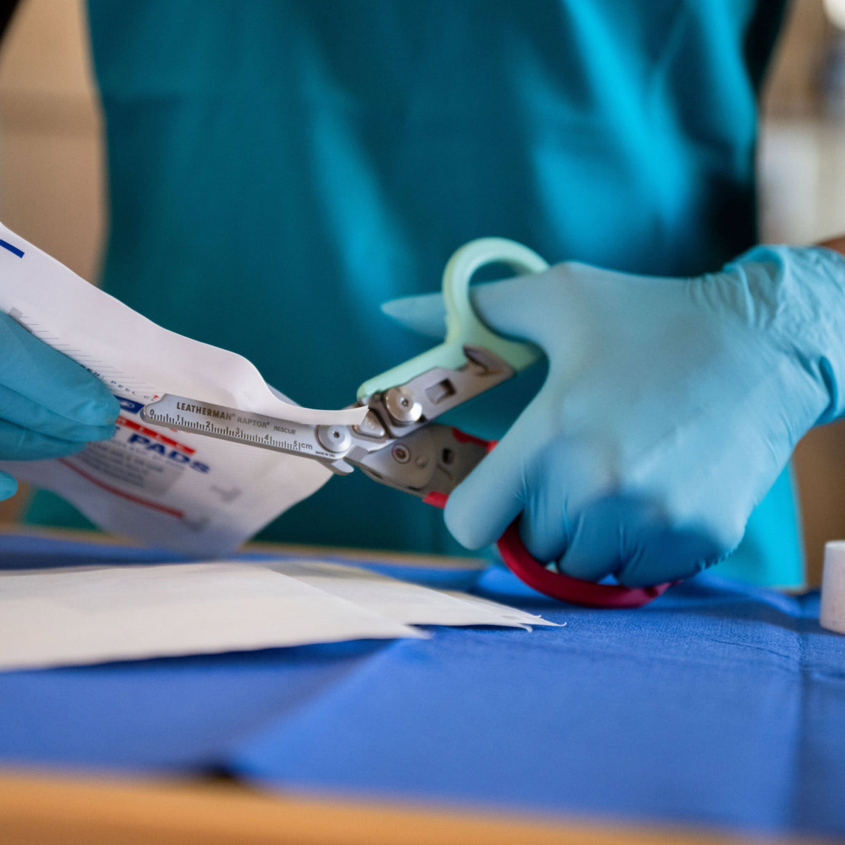 Translation missing: es.A nurse wearing blue gloves uses Leatherman South Beach Raptor Rescue shears to cut open the packaging of gauge carefully