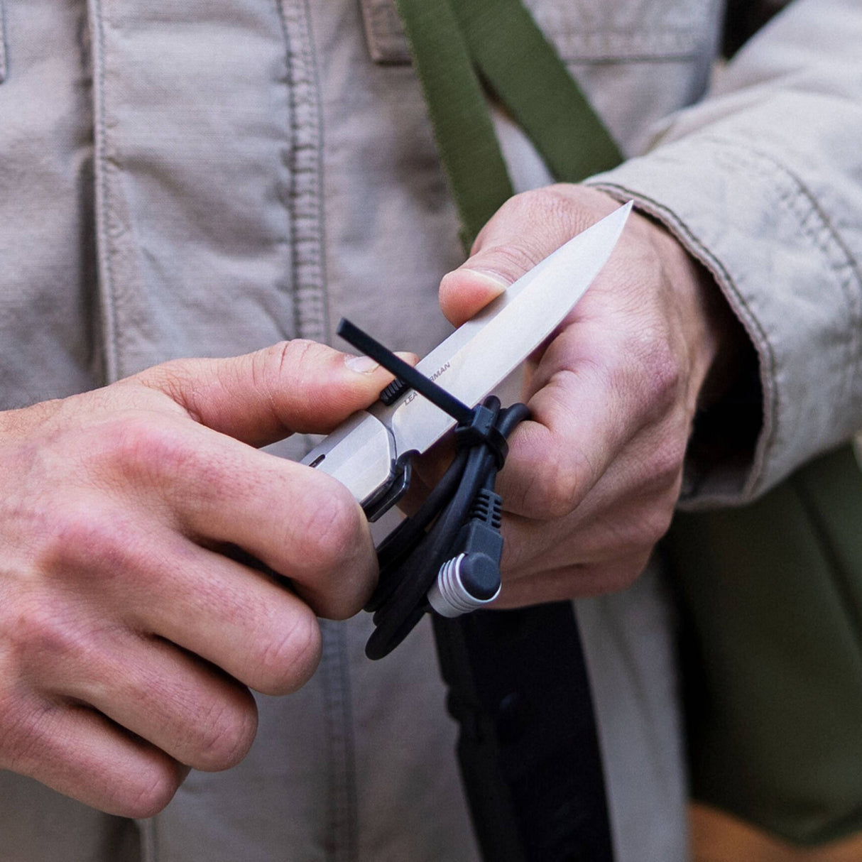 Translation missing: de.Person using a Leatherman Blazer Stainless Steel folding knife to cut a zip tie securing coiled cables, shown in a close-up with hands and utility jacket visible in an outdoor setting