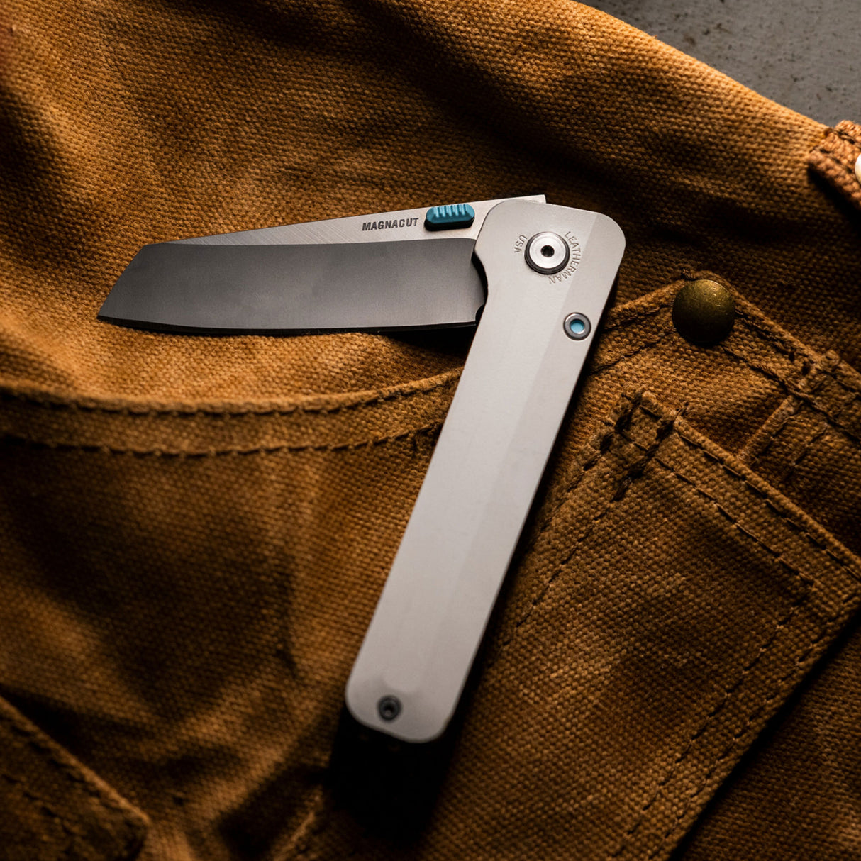 Translation missing: de.Leatherman Glider knife lies atop of brown Demin apron, creating a striking contrast between the tool and the fabric