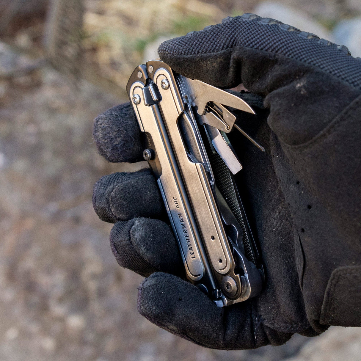 Translation missing: es.Black DLC & Stainless Steel Leatherman ARC® held in a gloved hand, showcasing some tool included tools