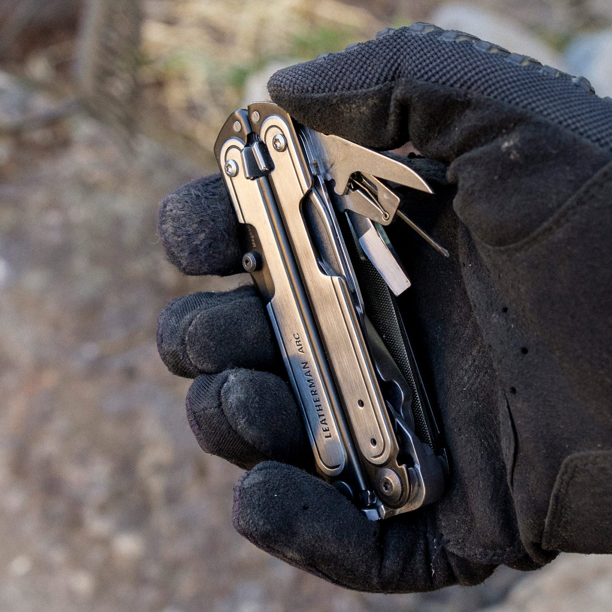 Translation missing: en.Black DLC & Stainless Steel Leatherman ARC® held in a gloved hand, showcasing some tool included tools