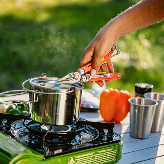 Translation missing: pl.A person cooks on a stove, using Leatherman Signal to handle a pot filled with food