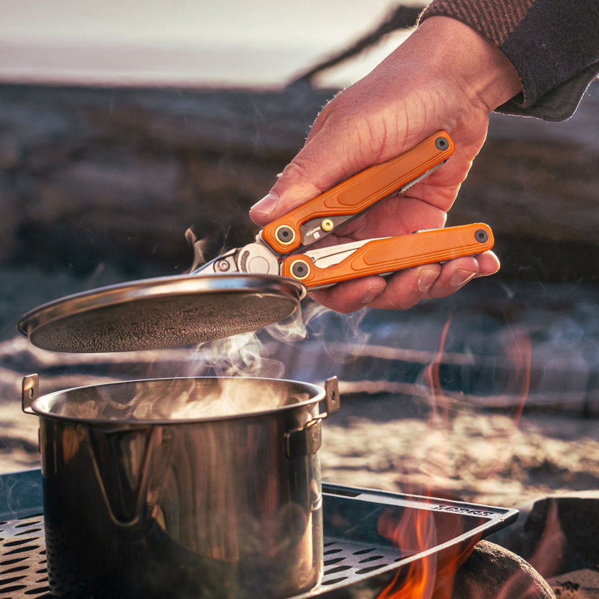 Translation missing: de.Person using Canyonland Leatherman Wave® Alpha multitool to remove a lid from a pot while camping outdoors