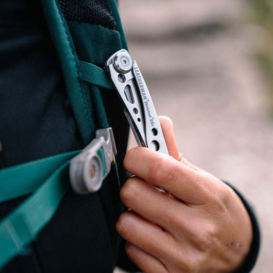 Translation missing: de.Person holding a closed Skeletool KBX that is attached to the strap of a backpack