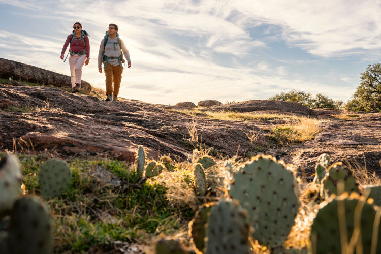 Translation missing: es.Two hikers wearing backpacks walking through a field