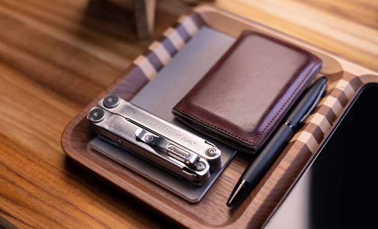 Translation missing: de.Leatherman Curl, dark brown leather wallet and black pen on top gray notepad nicely arrange on wooden tray