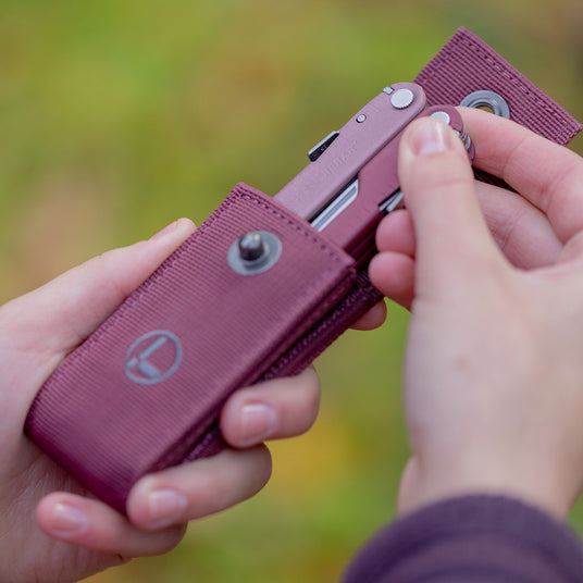 A close-up of a hand holding a Leatherman Bond, emphasizing the tool's design and sheath.