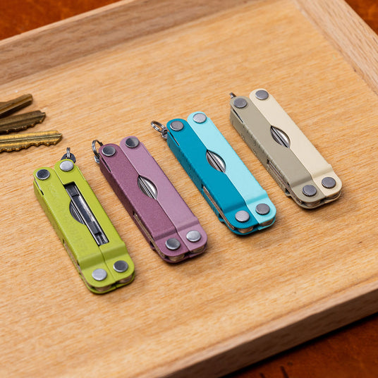 A wooden tray displaying five Leatherman Micras in various colors.