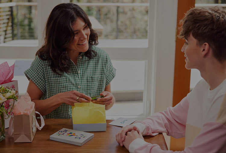 Translation missing: it.A mother opens Leatherman gift from son sitting at a table, capturing a moment of happiness and connection between them