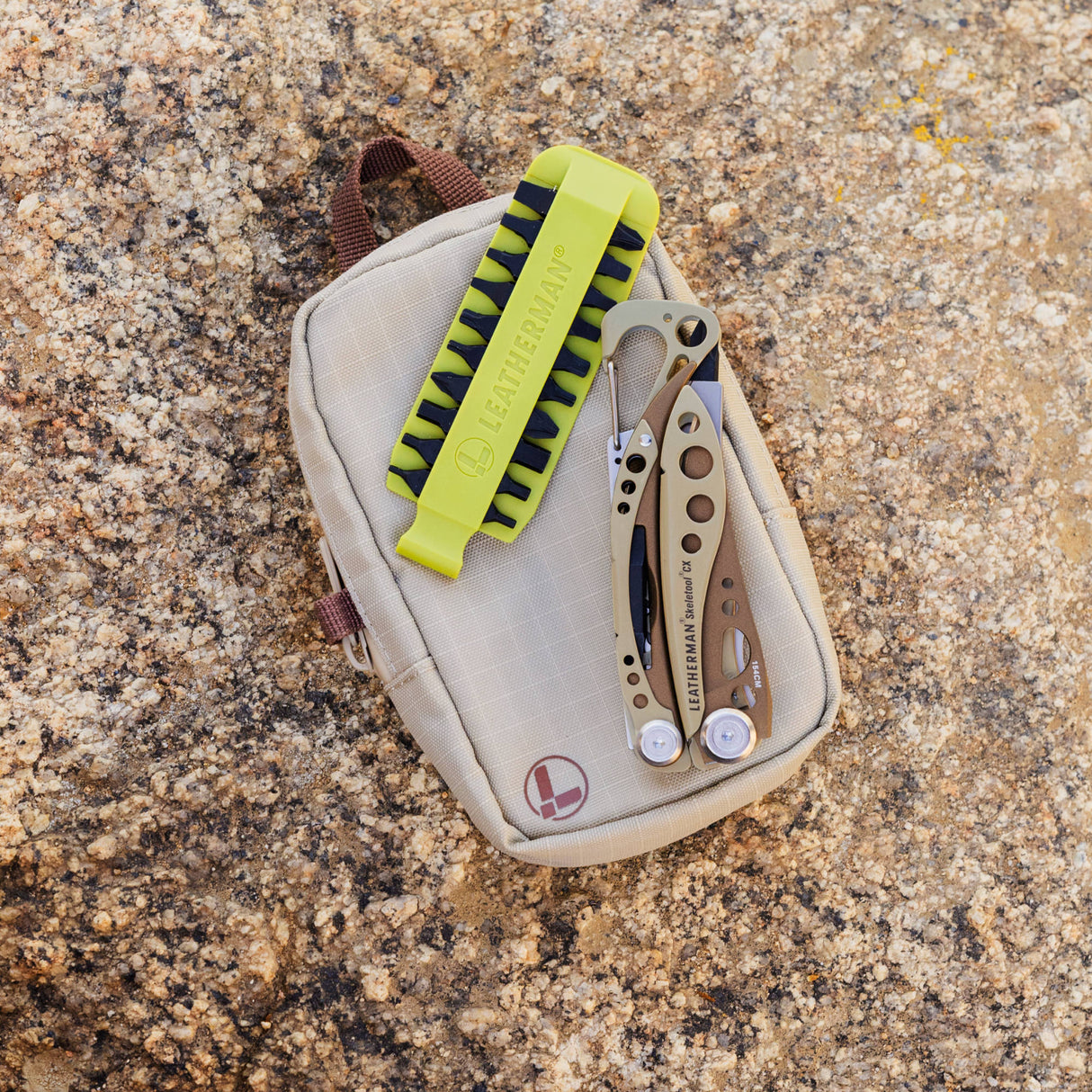 Translation missing: nl.Compact beige tool pouch with multitool and green Leatherman bit kit resting on rough rock outdoors