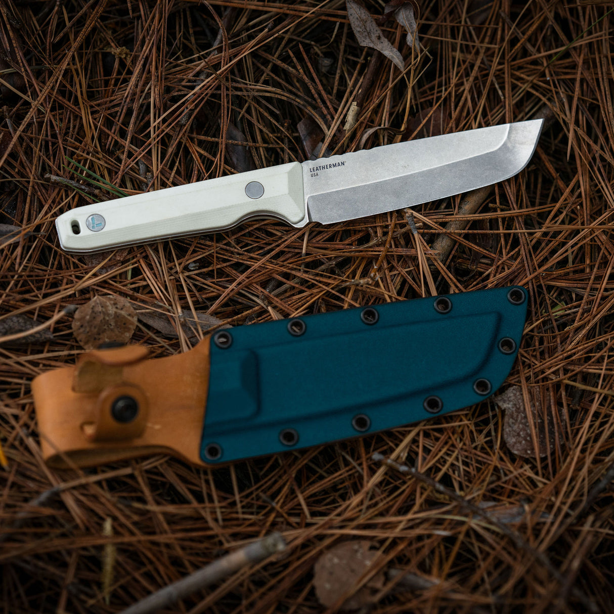 Translation missing: en.Alpine Leatherman Pioneer™ knife displayed on pine needles with its sheath in a natural outdoor setting