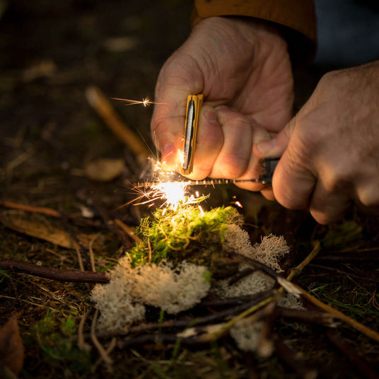 Translation missing: nl.Close-up hands using a Leatherman Signal to start a fire in the wilderness with a fire-starting ferro rod
