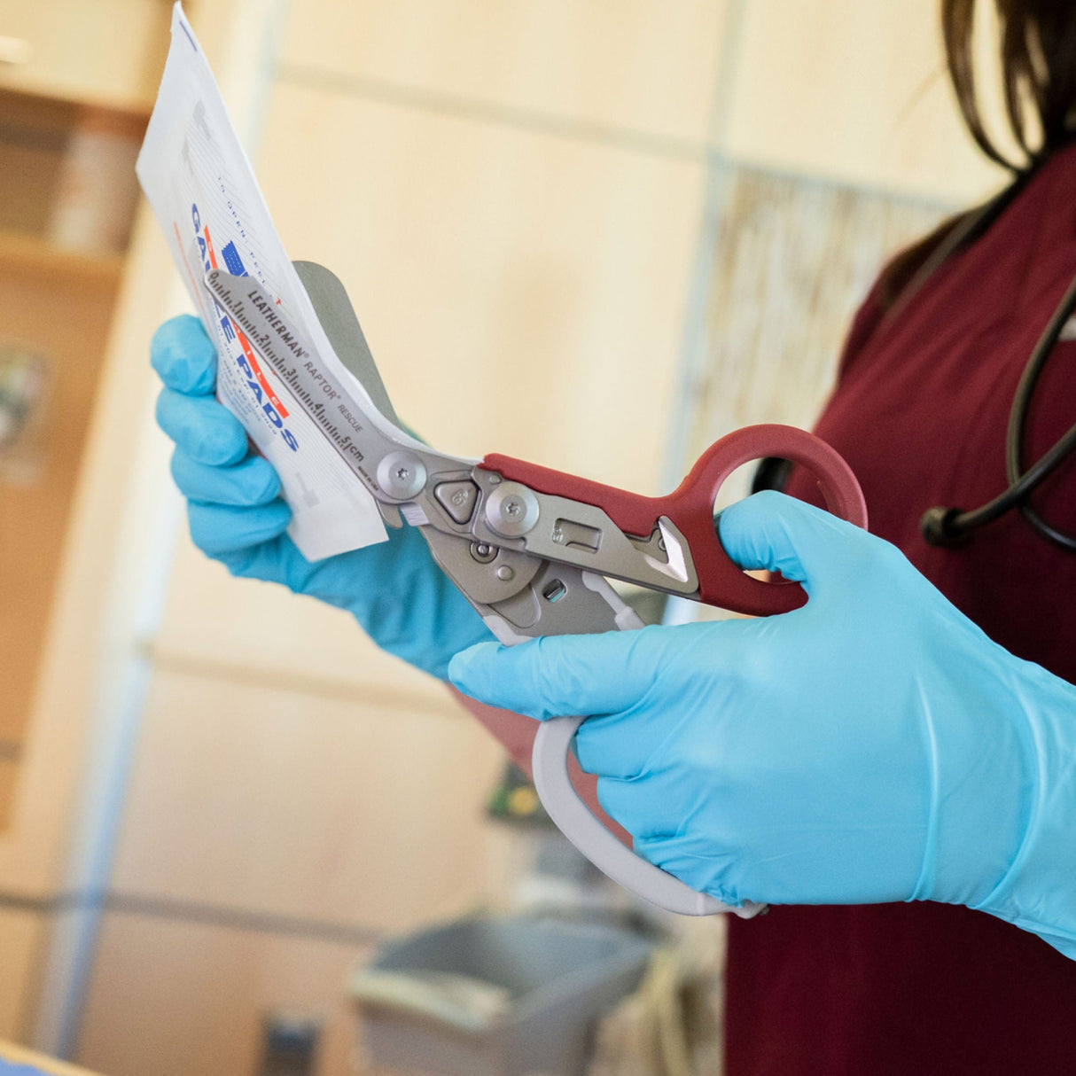 Translation missing: en.A nurse wearing blue gloves using the shears on a Garnet Leatherman Raptor® Rescue to cut open a package of gauge pads