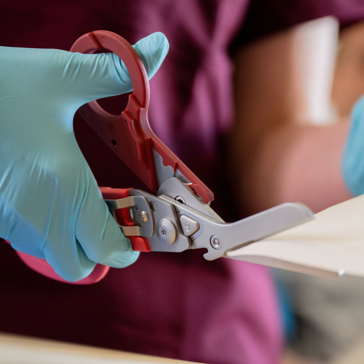 Translation missing: es.A nurse wearing blue gloves using the shears on a Raspberry Rose Leatherman Raptor® Rescue to cut gauze