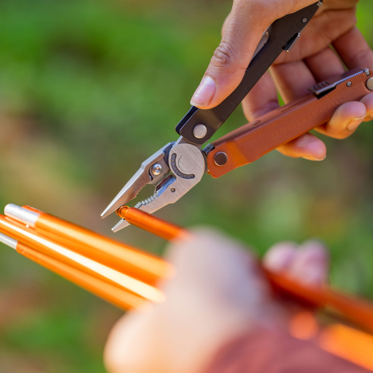 Translation missing: de.Hands using a Burnt Sienna Leatherman Rebar® multi-tool pliers to grip a tent stake, showcasing its functionality in outdoor settings