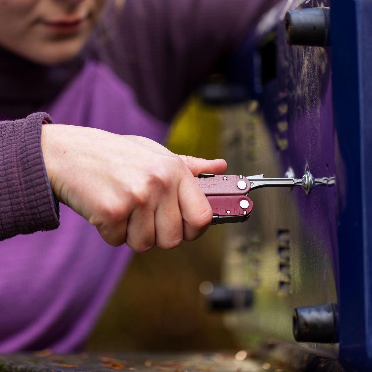 Translation missing: de.Person using a Heathered Cranberry Leatherman Rebar® multitool to tighten a screw outdoors