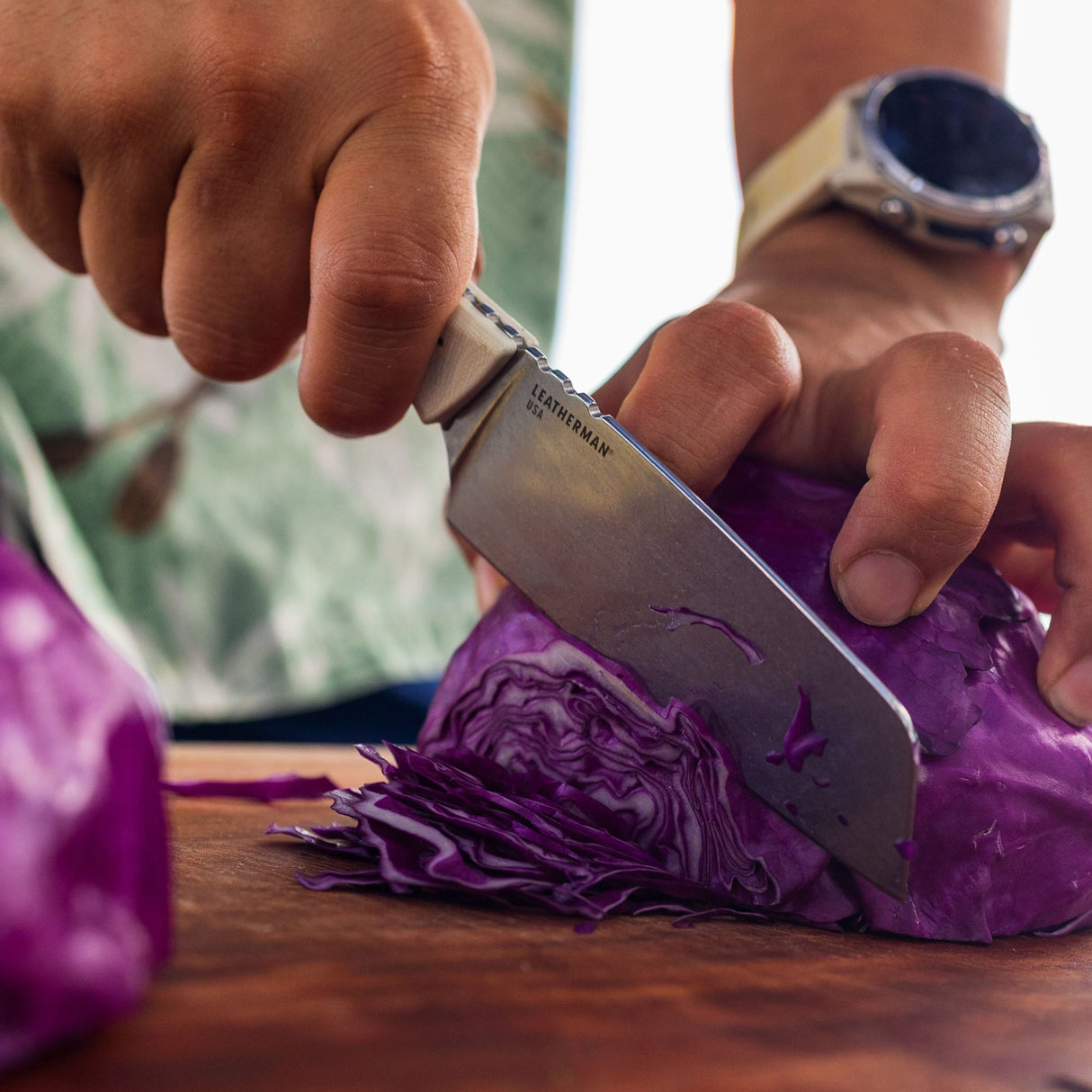 Translation missing: de.A person slicing purple cabbage on a wooden cutting board using a Leatherman Rustle Alpine knife