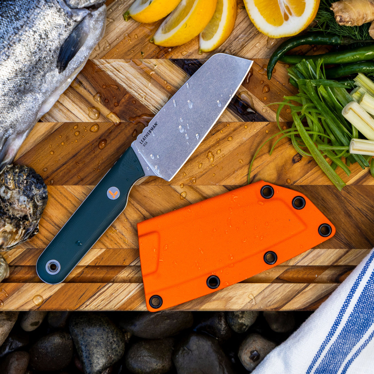 Translation missing: es.Leatherman Rustle Knife and sheath on block beside a colorful assortment of fresh vegetables on a wooden cutting board