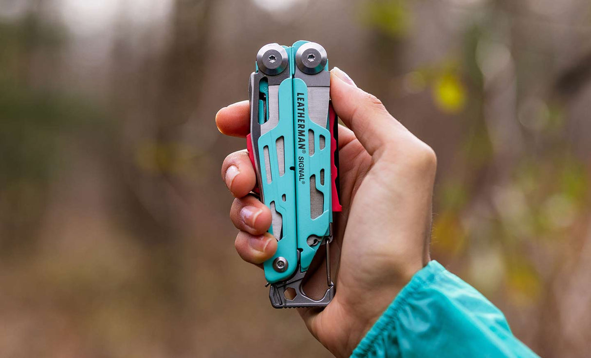 Translation missing: pl.Person holding an aqua and stainless Leatherman Signal® multi-tool in a natural outdoor setting