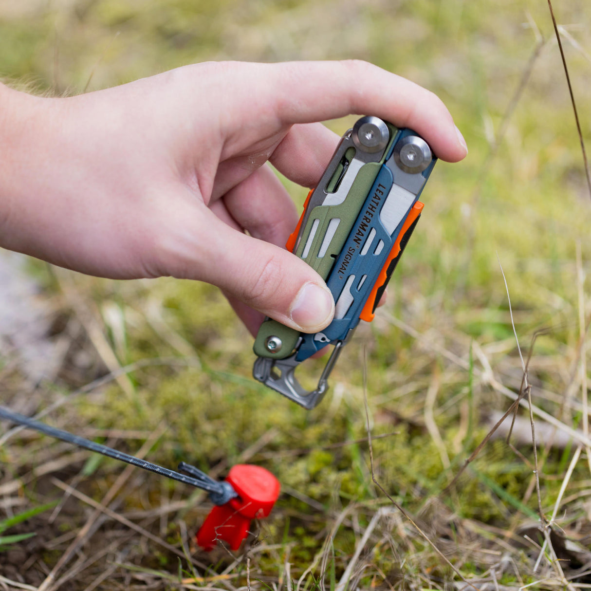 Translation missing: es.A person using the hammer on a Tundrascape Leatherman Signal® to hammer a tent stake in a patch of grass
