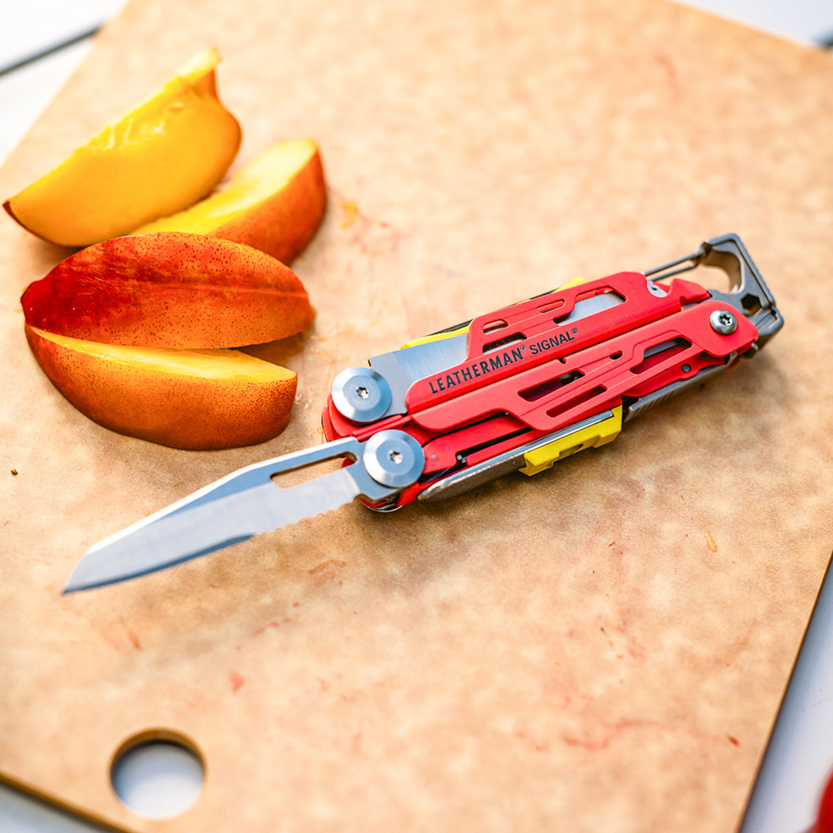Translation missing: es.Guava Leatherman Signal multitool with open serrated blade beside sliced peaches on a cutting board