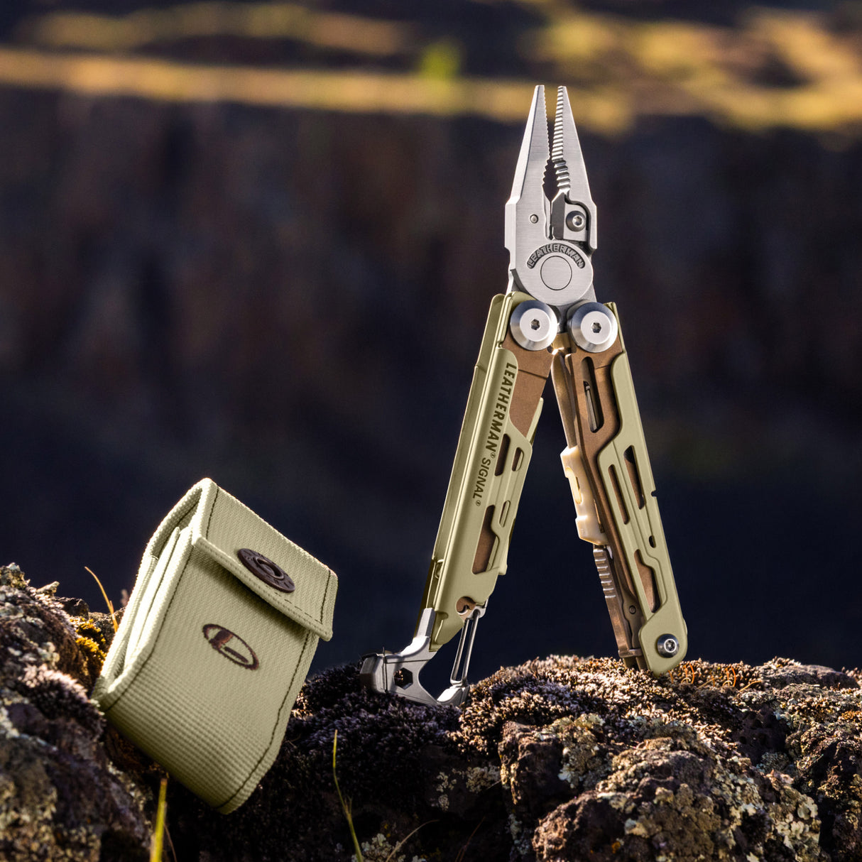 Translation missing: es.Sandstorm Leatherman Signal multitool with open pliers and matching case resting on rocky terrain outdoors