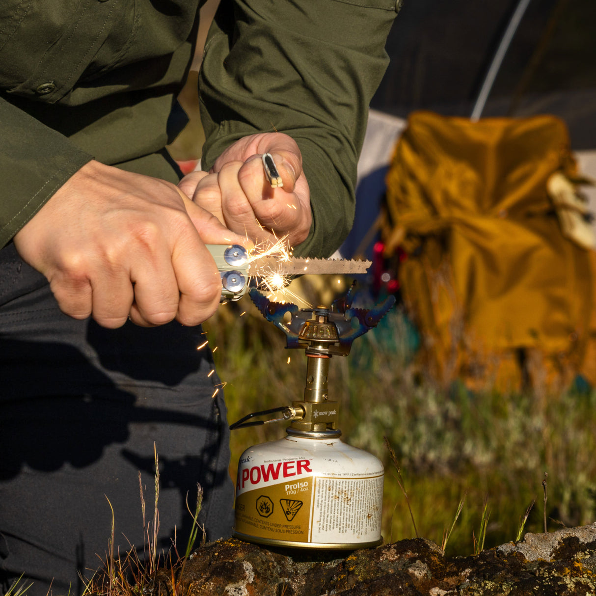 Translation missing: es.Hands using a Sandstorm multitool to strike sparks onto a small camping stove outdoors