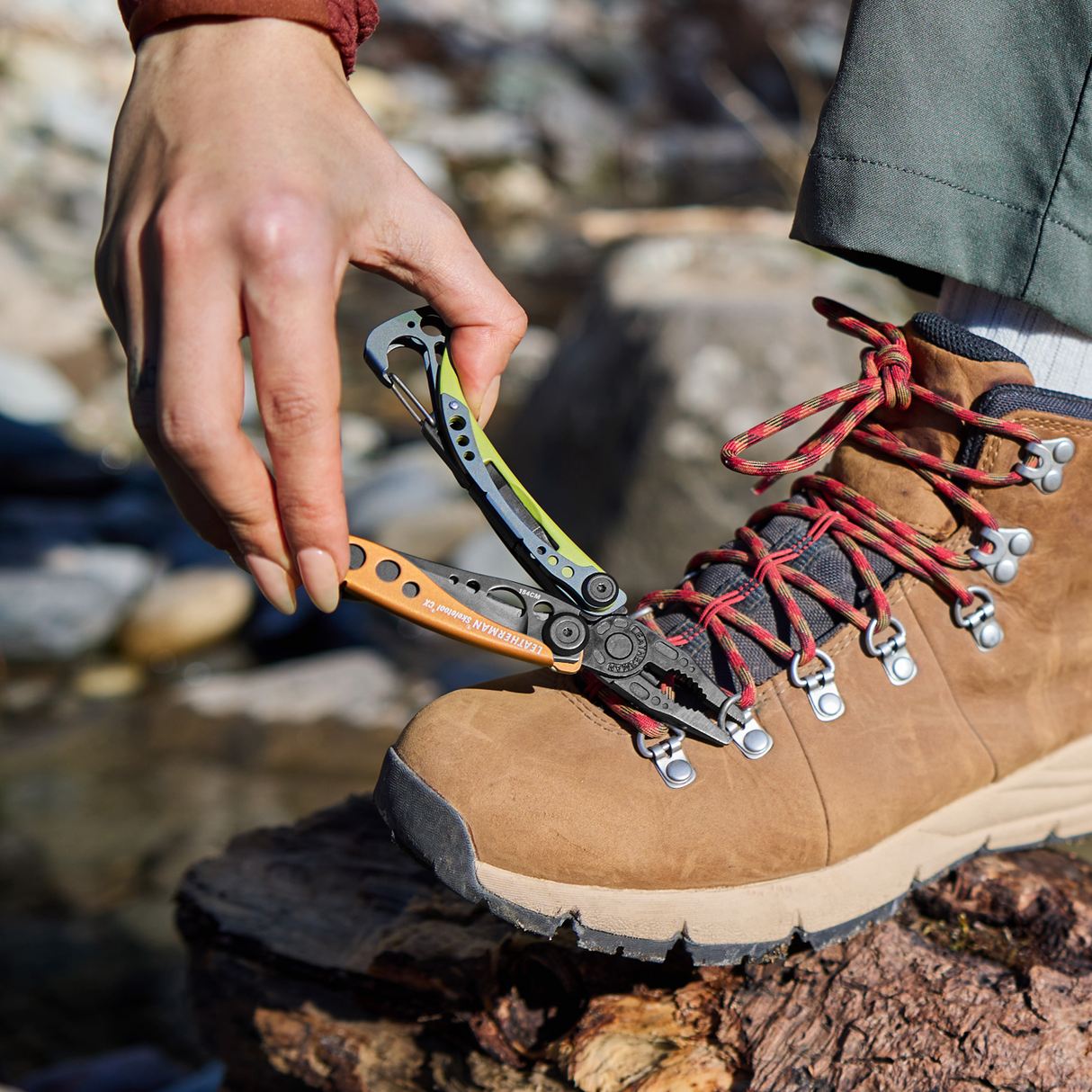 Translation missing: de.Person using a Leatherman Skeletool® CX in Aurora color to fix the lace hook on a hiking boot