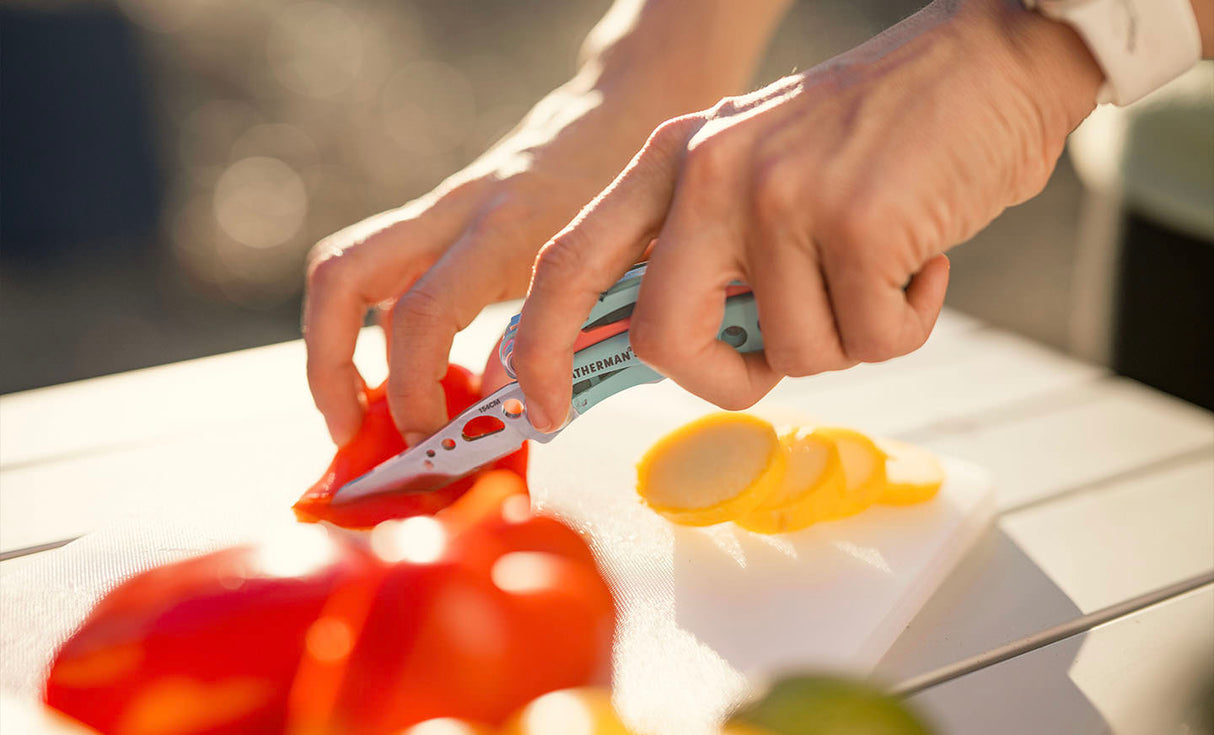 Translation missing: es.Person using a Paradise Leatherman Skeletool® CX to slice colorful vegetables on a cutting board outdoors