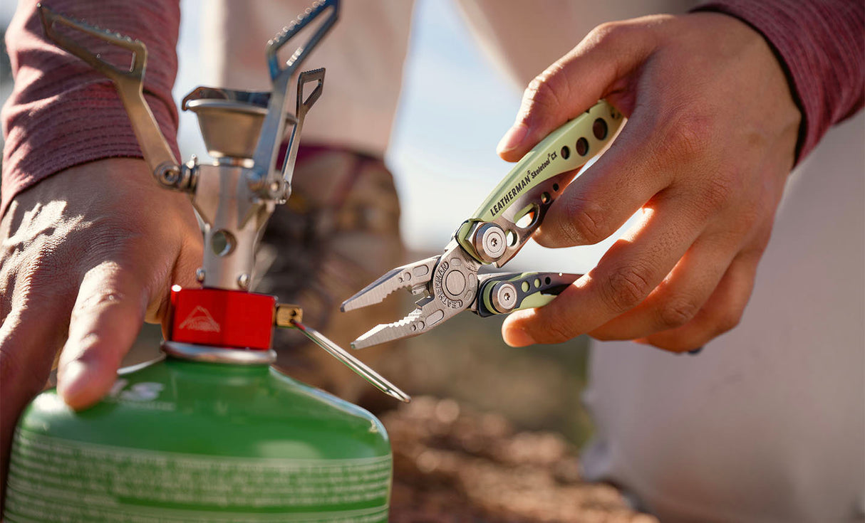 Translation missing: es.Person using a Verdant Leatherman Skeletool® CX multi-tool to adjust a camping stove on a green propane canister
