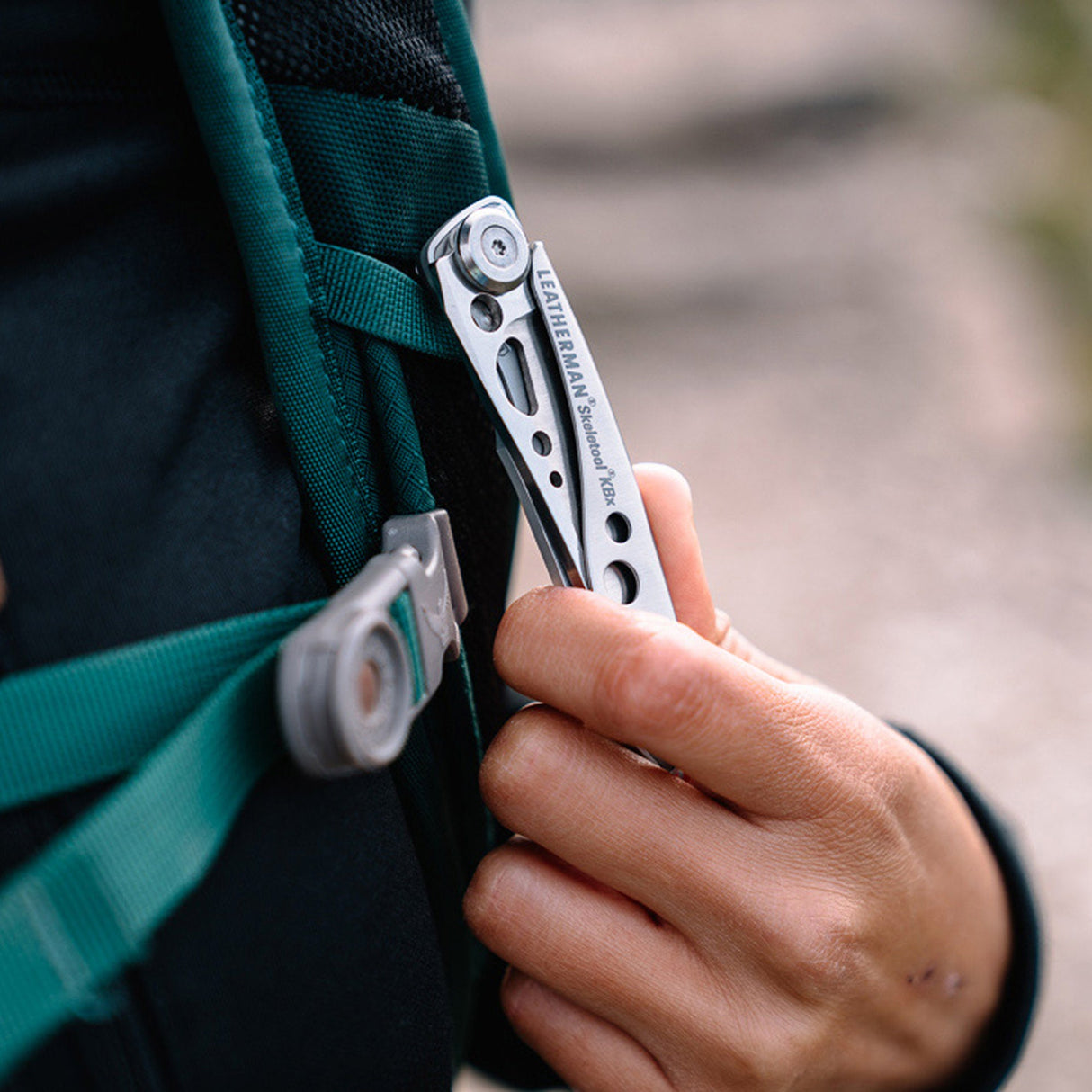 Translation missing: pl.Hand clipping a stainless steel Skeletool KBX pocket knife onto a backpack strap