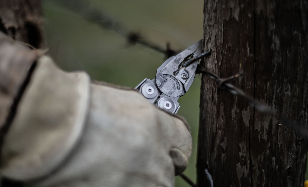 Translation missing: es.Person using a stainless steel Leatherman Surge® multitool pliers on barbed wire attached to a wooden post