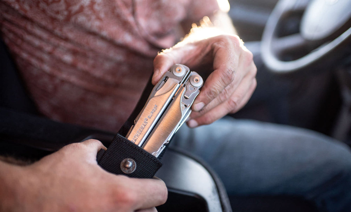 Translation missing: es.Person pulling a stainless steel Leatherman Surge® multitool from its sheath while sitting in a car