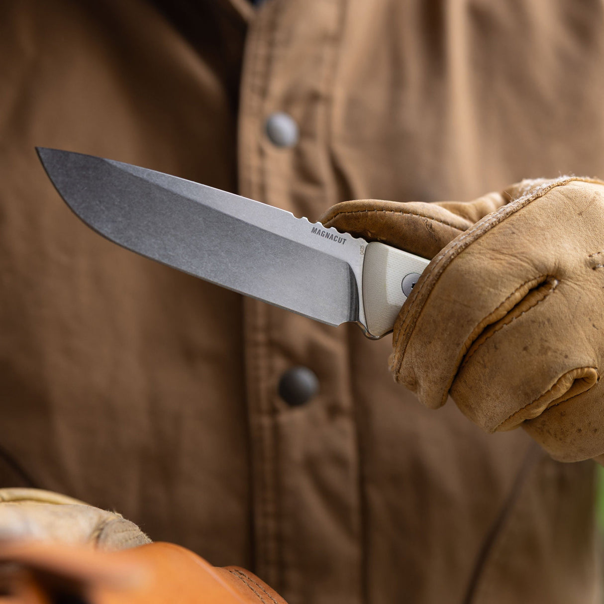 Translation missing: de.Person wearing work gloves and a brown canvas jacket holding a Leatherman Trac Alpine fixed-blade knife outdoors, emphasizing the blade and handle in a close-up view