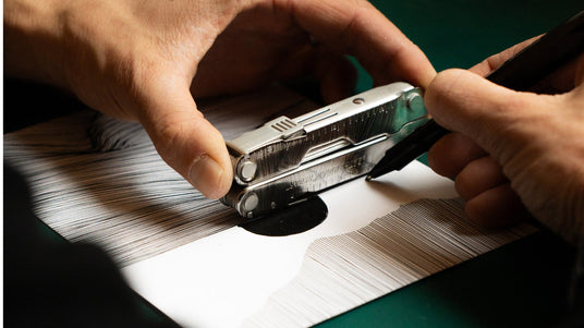 Translation missing: en.Person using the ruler on a stainless steel Leatherman Rebar to draw lines on a piece of paper