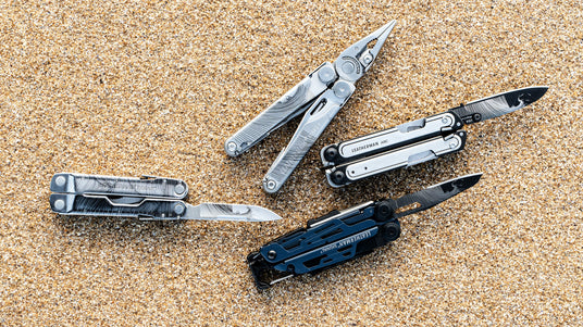 Translation missing: en.Four customized Leatherman multitools arranged on sandy surface, showcasing their unique designs and features