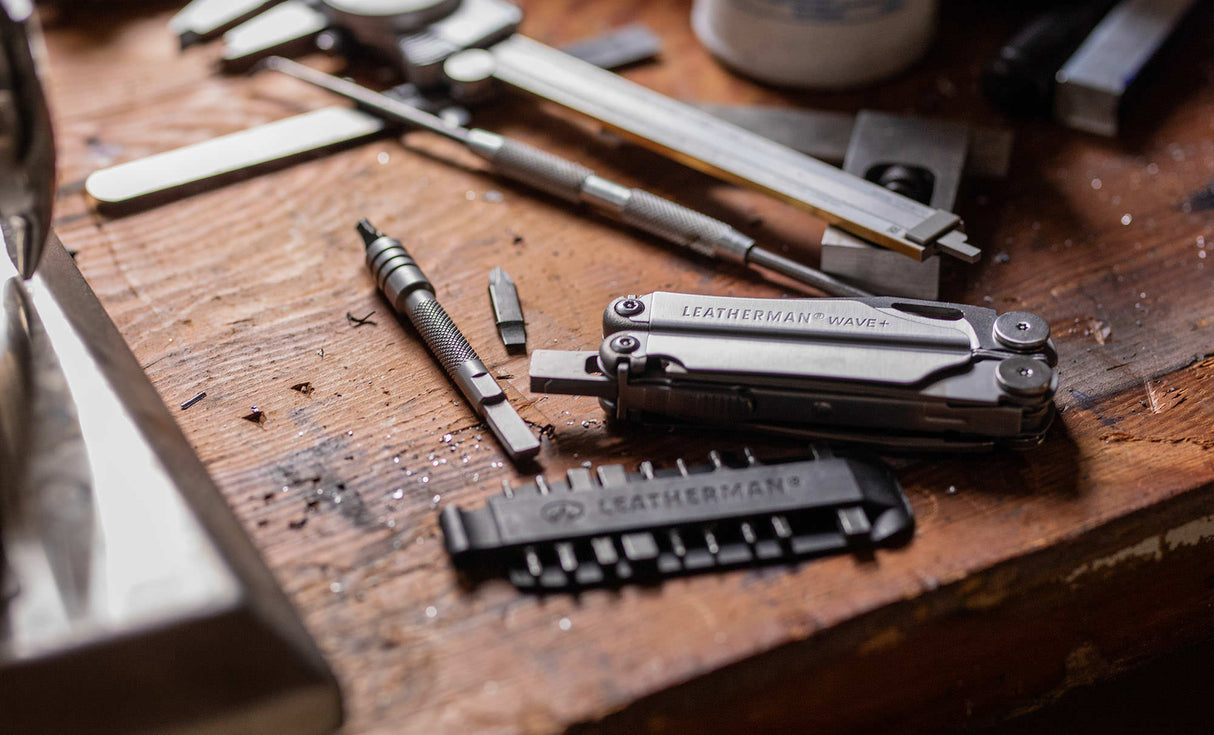 Translation missing: es.Stainless Steel Leatherman Wave® Plus multi-tool on a workbench alongside a Leatherman bit kit, bit and bit driver extender