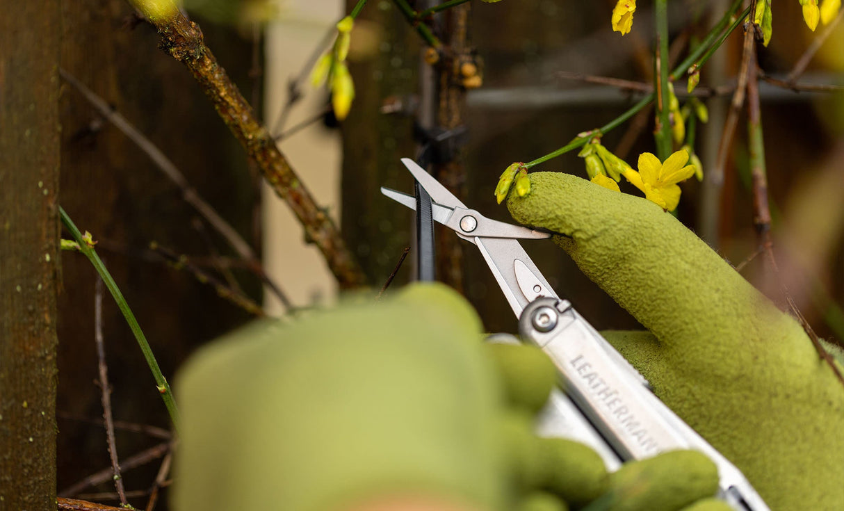 Translation missing: es.Close-up of hands using a Stainless Steel Leatherman Wave® Plus scissors to cut a zip tie in a garden