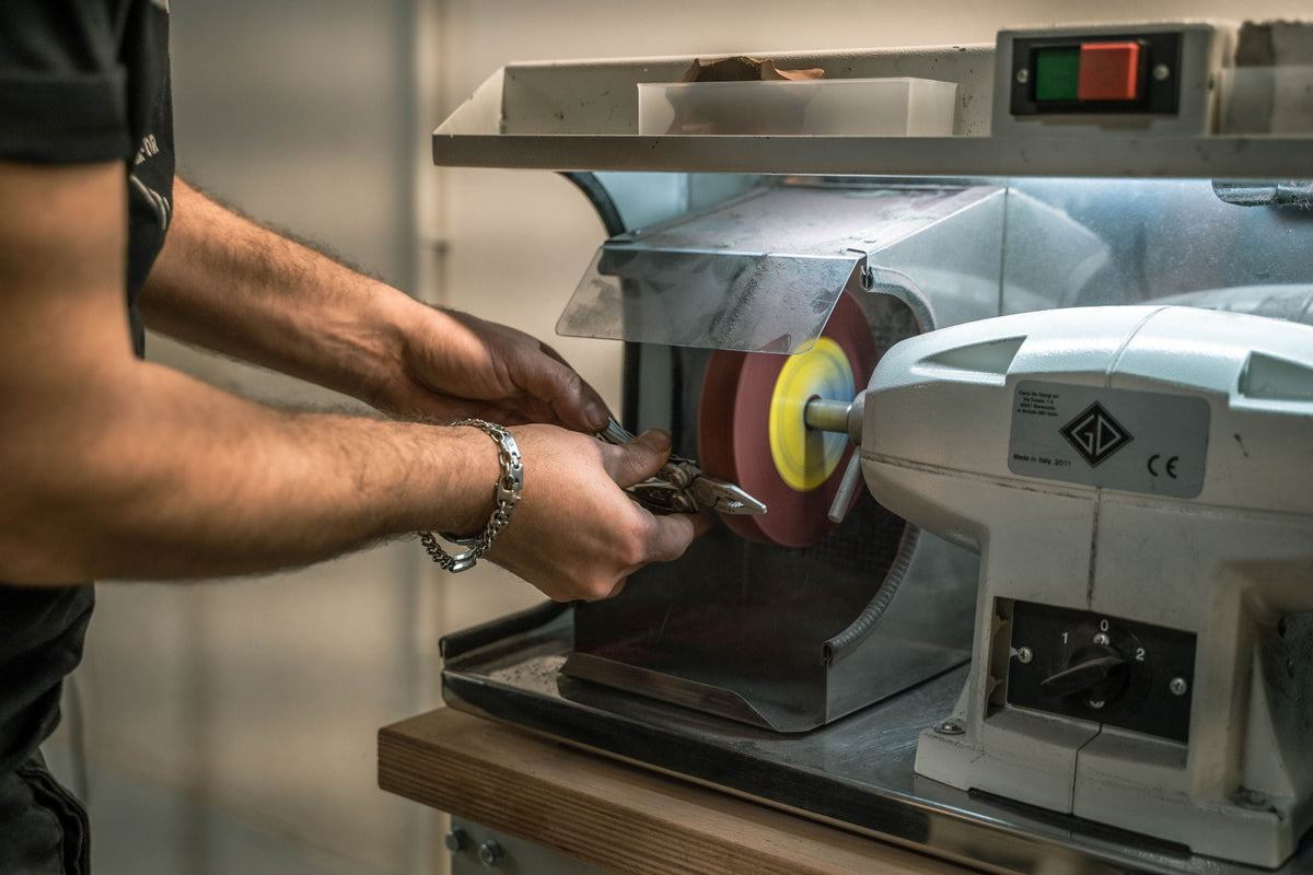 Technician sharpening a Leatherman multi-tool on a workshop grinding wheel as part of the 25-year warranty repair process.