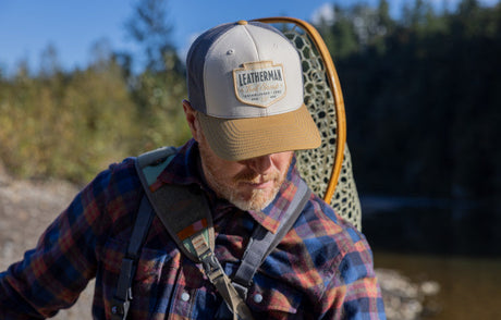 Translation missing: es.Man wearing a Leatherman Pacific Northwest Trucker hat walking alongside a stream carrying a backpack and net