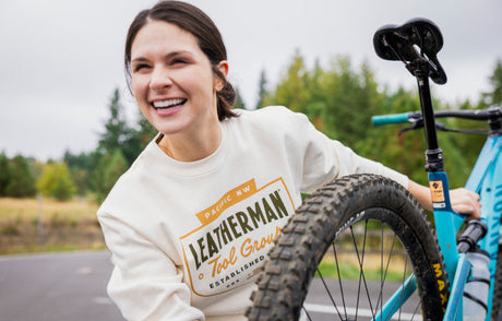 Translation missing: es.Woman wearing a Leatherman Pacific Northwest crewneck, standing next to a bicycle outdoors